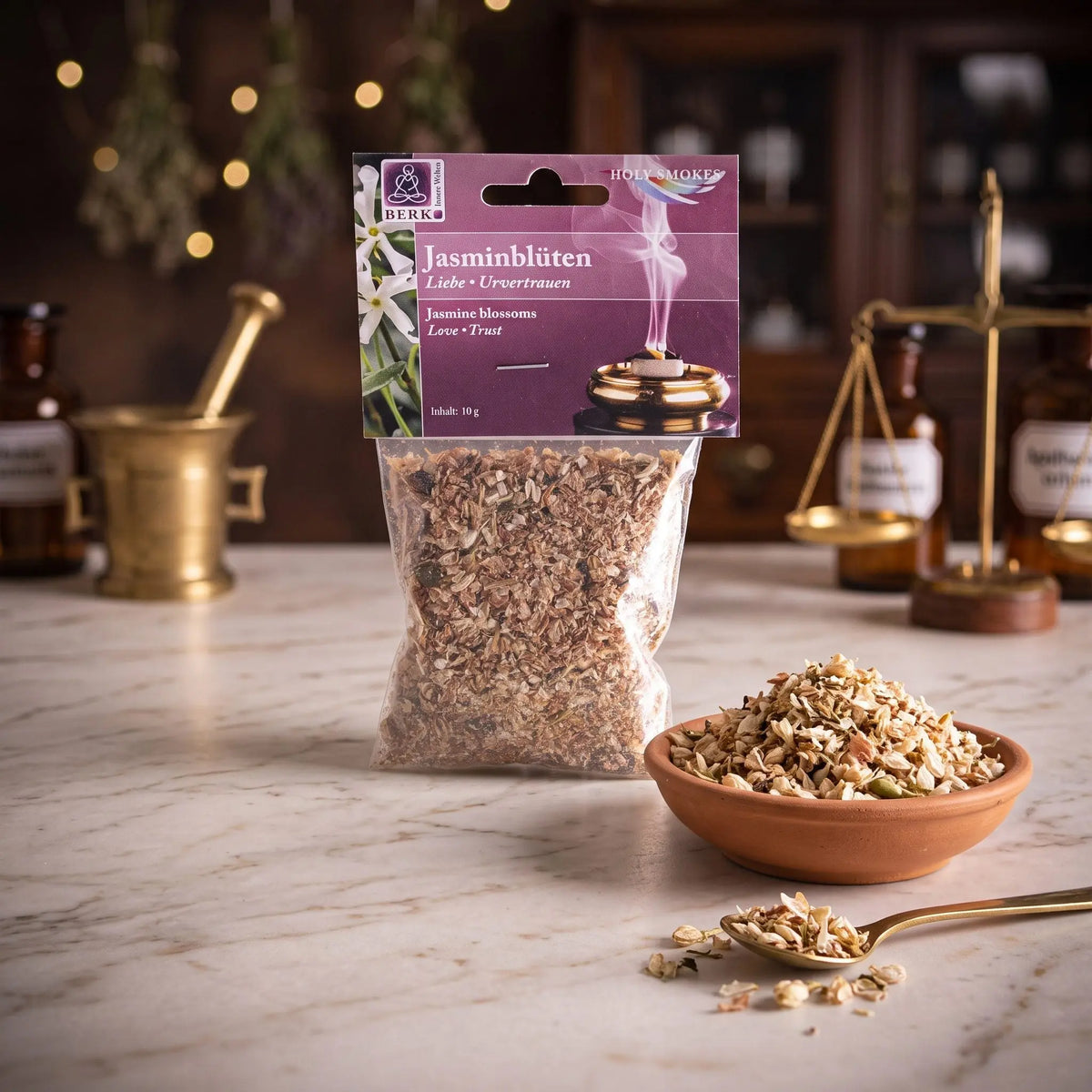 Jasminblüten, sortenreines Räucherwerk von Berk, 10 g: Packung auf der Marmortheke einer alten Apotheke am Abend, daneben eine Terracottaschale mit getrockneten Jasminblüten und ein Messinglöffel – Spirit of Gaia