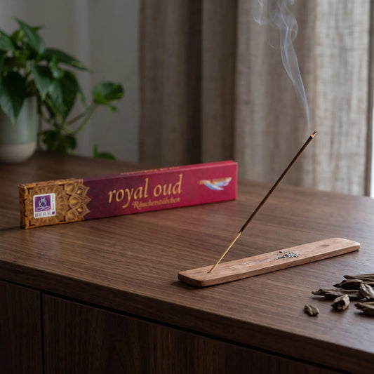 Räucherstäbchen Royal Oud von Berk: glimmendes Räucherstäbchen mit feinem Rauch im Holzhalter, dahinter die Packung, auf einem Sideboard am Abend