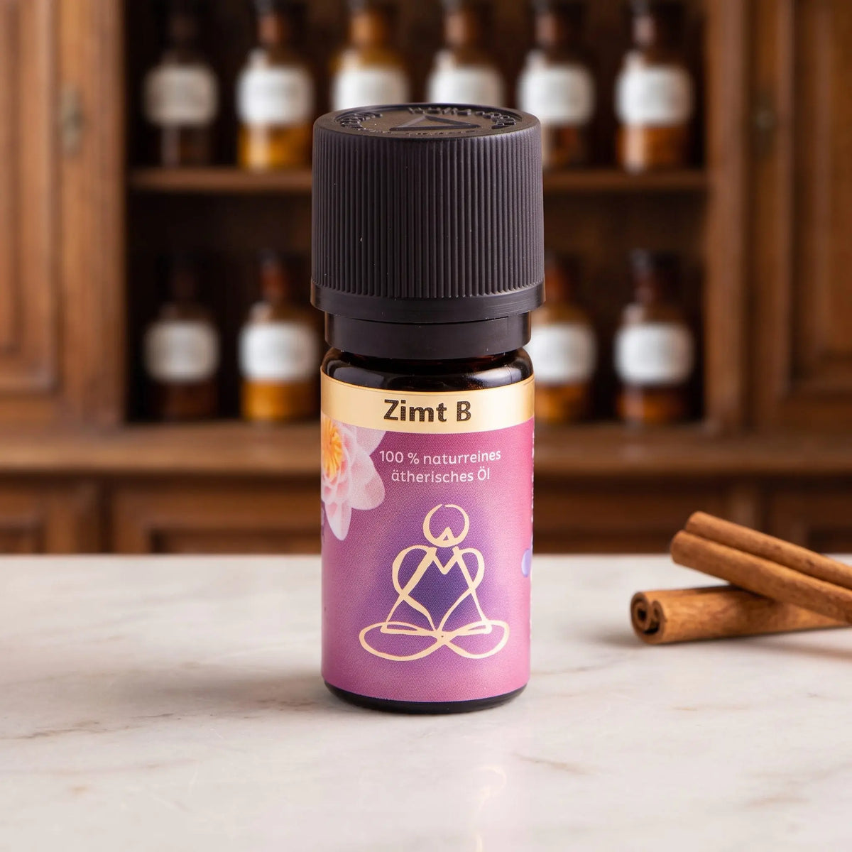 Ätherisches Öl Zimt: Fläschchen aus Braunglas auf Marmortheke vor Apothekerschrank, daneben Zimtstangen – Spirit of Gaia