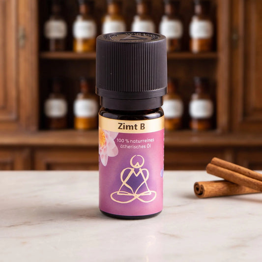 Ätherisches Öl Zimt: Fläschchen aus Braunglas auf Marmortheke vor Apothekerschrank, daneben Zimtstangen – Spirit of Gaia