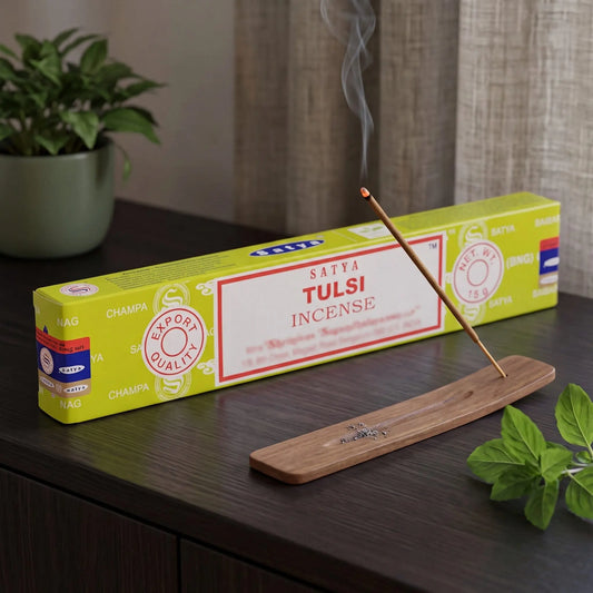 Satya Tulsi Räucherstäbchen: glimmendes Räucherstäbchen mit feinem Rauch im Holzhalter, dahinter die Packung, auf einem Sideboard am Abend