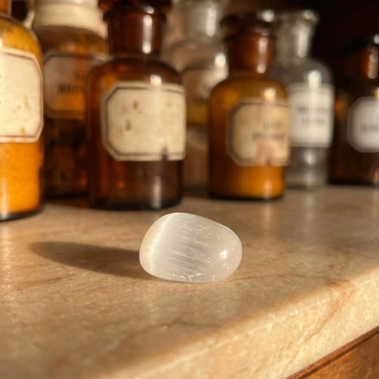 Selenit Trommelstein – milchweißer Heilstein mit seidigem Schimmer auf antiker Apotheker-Marmorablage
