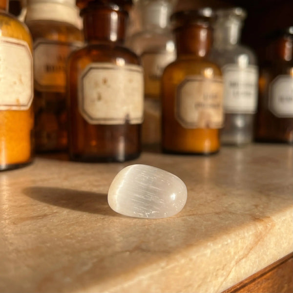 Selenit Trommelstein – milchweißer Heilstein mit seidigem Schimmer auf antiker Apotheker-Marmorablage