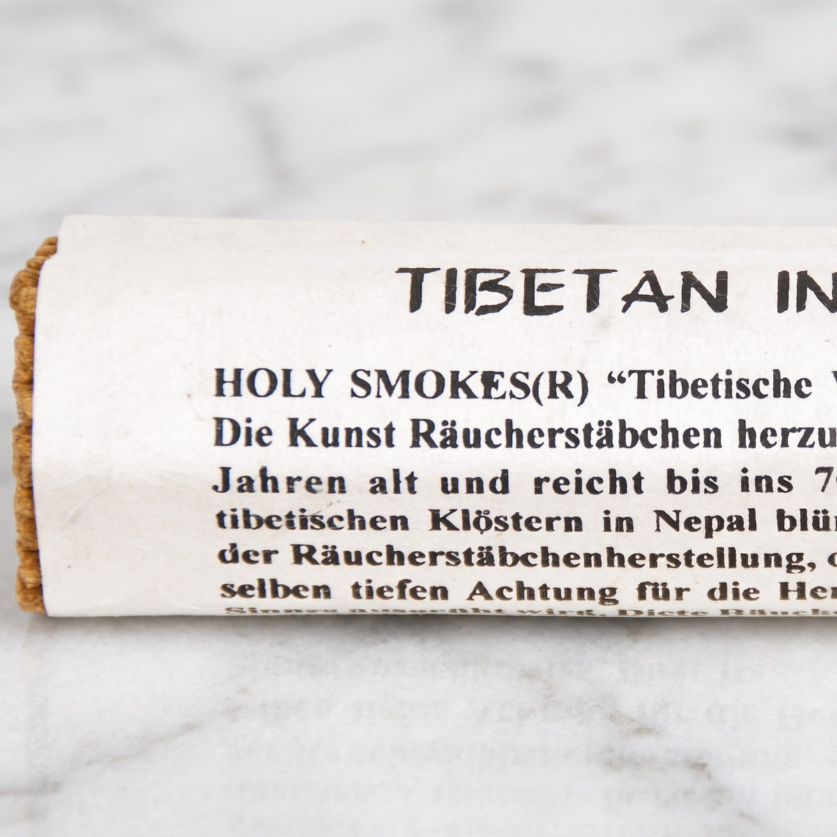 Nahaufnahme der Papierrolle mit Aufdruck Tibetan Incense und Holy Smokes und den ockerbraunen Stäbchenenden auf Marmor