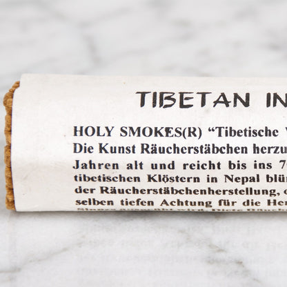 Nahaufnahme der Papierrolle mit Aufdruck Tibetan Incense und Holy Smokes und den ockerbraunen Stäbchenenden auf Marmor