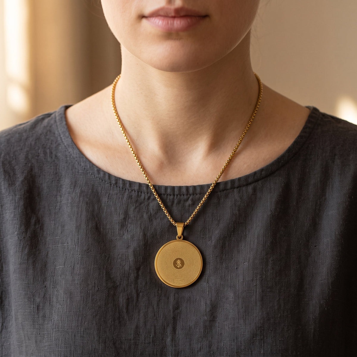 Vergoldeter Mantra Anhänger mit OM an 60 cm Kette auf dem Brustbein, dunkles Leinenoberteil