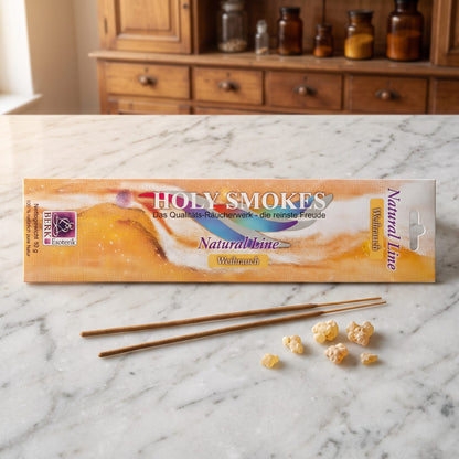 Weihrauch Räucherstäbchen der Holy Smokes Natural Line von Berk: flache Packung auf einer Marmortheke vor einem alten Holzschrank mit Schubladen und Bernsteinglasflaschen, davor zwei lose Stäbchen und ein paar Weihrauchharz-Tränen