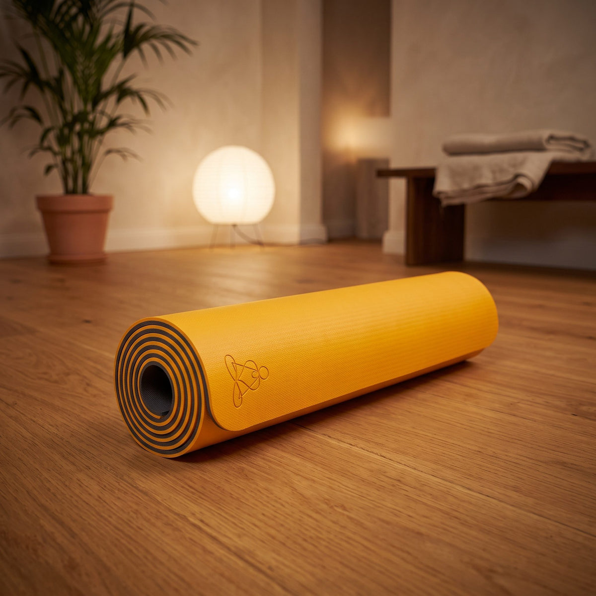 EcoBalance Yogamatte aus TPE, 182 × 61 cm, 6 mm, Blume des Lebens, orange/grau: eingerollt auf dem Holzboden eines ruhigen Meditationsraums am Abend – Spirit of Gaia