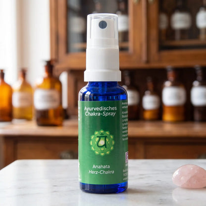 Ayurvedisches Chakra-Spray Anahata (Herz-Chakra): 30-ml-Sprühflasche aus blauem Glas auf Marmortheke vor Apothekerschrank, daneben Rosenquarz – Spirit of Gaia