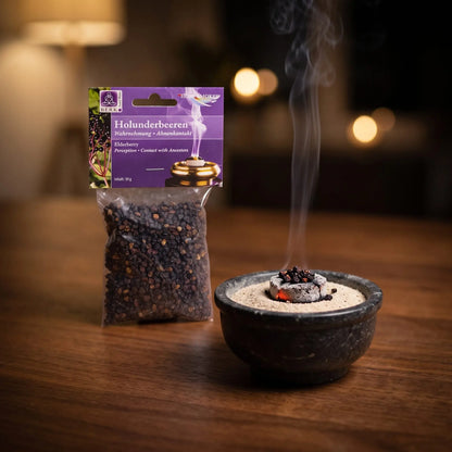 Holunderbeeren, sortenreines Räucherwerk von Berk, 30 g: einige Holunderbeeren glimmen auf der Räucherkohle, dahinter die Tüte, feiner Rauch steigt auf einer dunklen Holzplatte am Abend auf – Spirit of Gaia