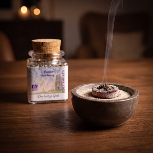 Der heilige Gral, Avalon-Räuchermischung von Berk, 50 ml im Korkglas: glimmende Räucherkohle mit einer Prise Räucherwerk in einer Specksteinschale, dahinter das Korkglas, feiner Rauch steigt auf einer dunklen Holzplatte am Abend auf – Spirit of Gaia