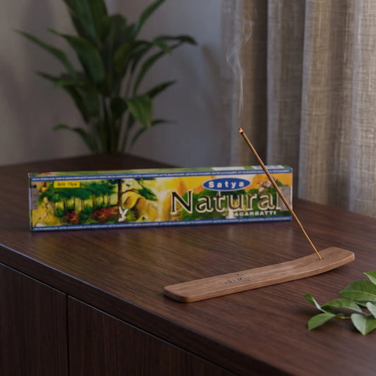 Satya Natural Räucherstäbchen: glimmendes Räucherstäbchen mit feinem Rauch im Holzhalter, dahinter die Packung, auf einem Sideboard am Abend