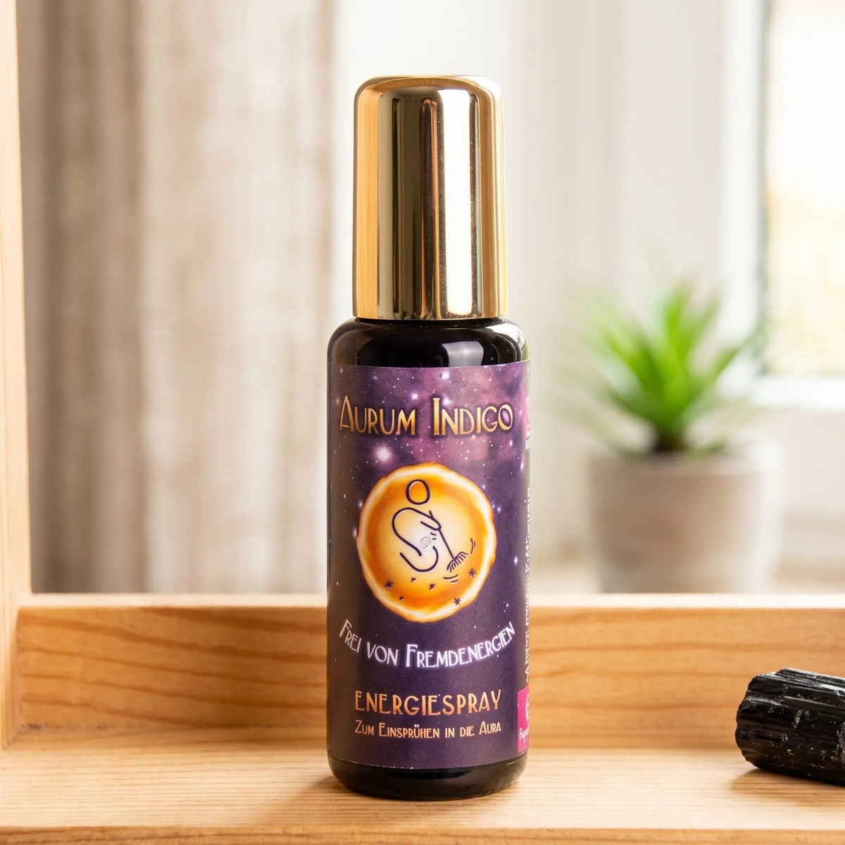 Energiespray Aurum Indigo Frei von Fremdenergien: Sprühflasche auf einem hellen Holzregal am Fenster mit Leinenvorhang, daneben ein schwarzer Turmalin