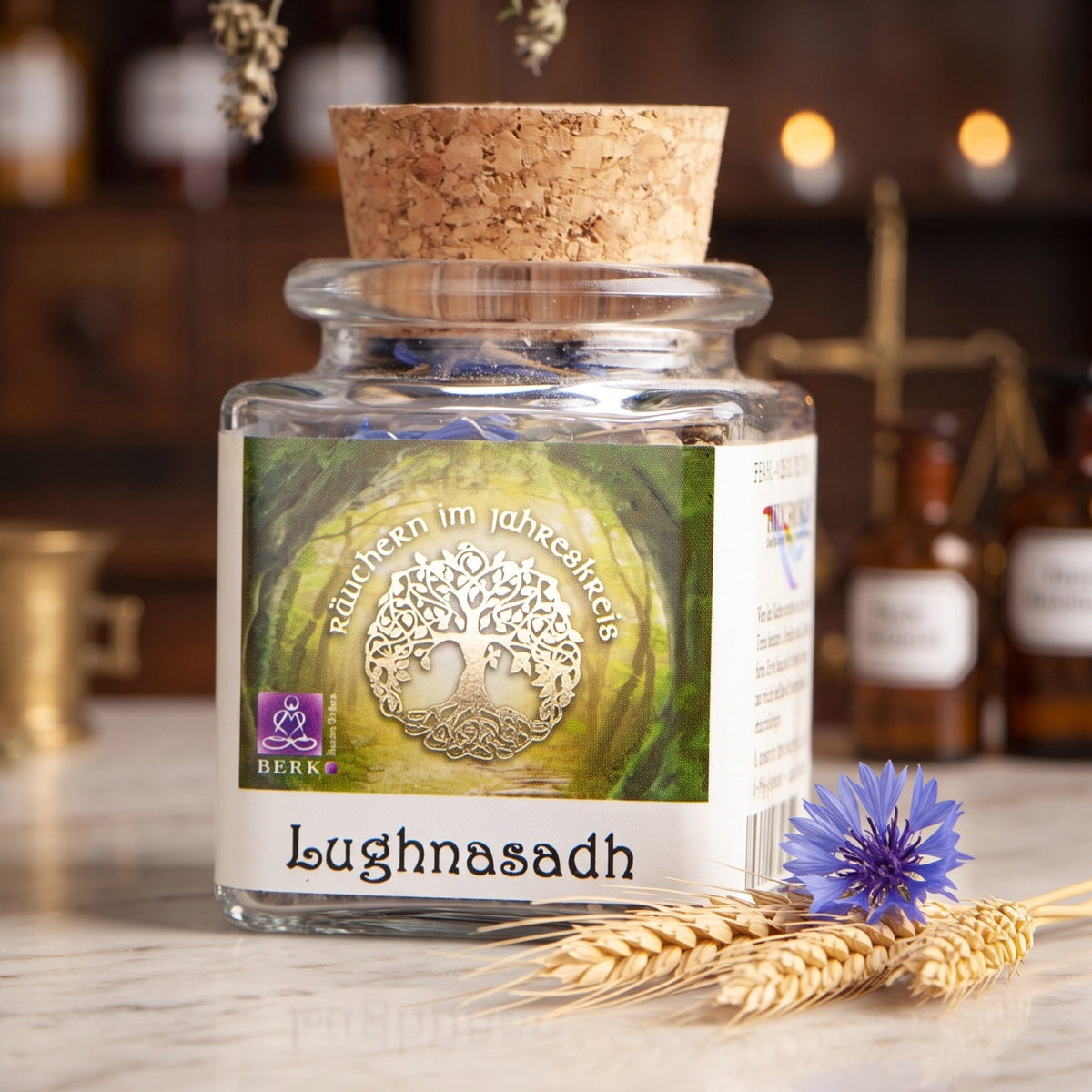 Lughnasadh, Jahreskreisfeste-Räuchermischung von Berk, 50 ml im Korkglas: Korkglas auf der Marmortheke einer alten Apotheke am Abend, daneben drei Weizenähren und eine Kornblume – Spirit of Gaia