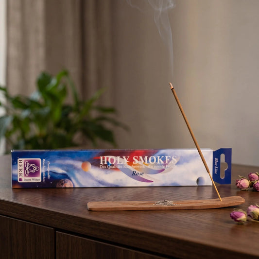 Rose Räucherstäbchen Blue Line: glimmendes Räucherstäbchen mit feinem Rauch im Holzhalter, dahinter die Packung, auf einem Sideboard am Abend