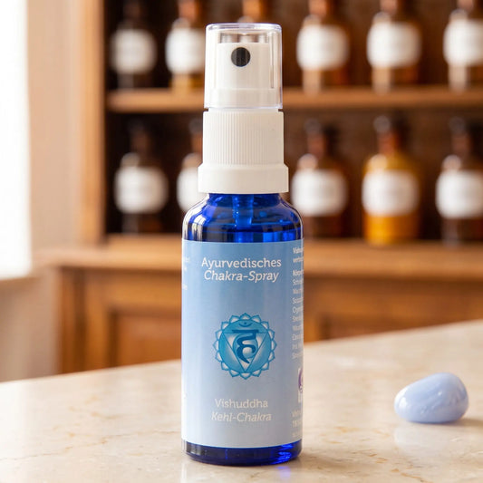 Ayurvedisches Chakra-Spray Vishuddha (Kehl-Chakra): 30-ml-Sprühflasche aus blauem Glas auf Marmortheke vor Apothekerschrank, daneben blauer Chalcedon – Spirit of Gaia
