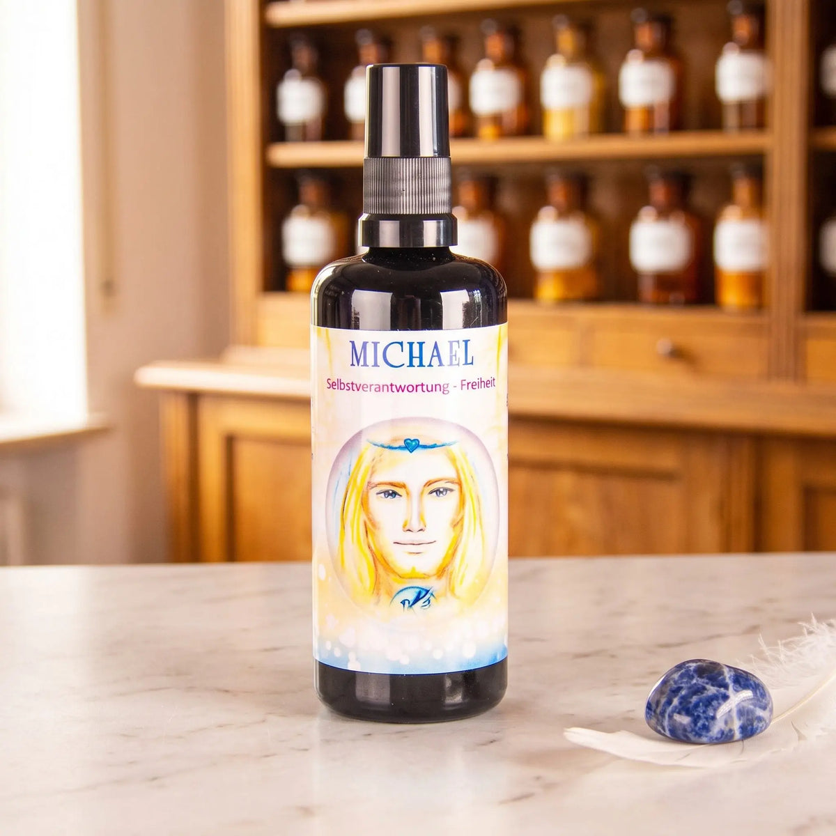 Seraphim Engel-Essenz Michael: Aura-Spray in dunkler Violettglasflasche auf Marmortheke vor Apothekerschrank, daneben ein Sodalith und eine weiße Feder – Spirit of Gaia