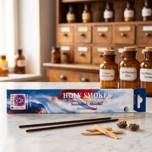 Sandelholz Moschus Räucherstäbchen Holy Smokes Blue Line: Packung auf einer Marmortheke vor einem Apothekerschrank, davor zwei lose Räucherstäbchen und Sandelholzspäne und dunkle Harzstücke – Spirit of Gaia