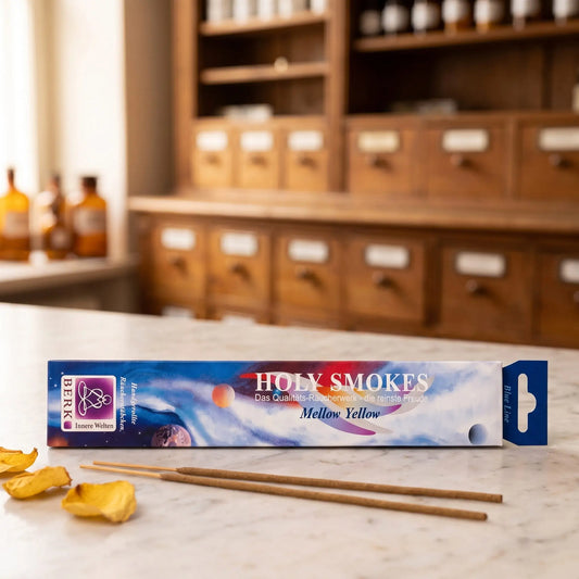 Mellow Yellow Räucherstäbchen Blue Line: Packung auf einer Marmortheke vor einem Apothekerschrank, daneben zwei lose Räucherstäbchen und ein paar getrocknete gelbe Rosenblätter – Spirit of Gaia
