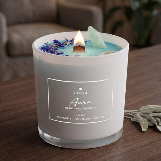 Zeremonie Kerze Aurareinigung mit Aventurin, Duft Salbei und Maiglöckchen: brennende Kerze mit kleiner Flamme am Abend auf einer dunklen Holzplatte im Wohnzimmer, daneben ein paar getrocknete Salbeiblätter – Spirit of Gaia
