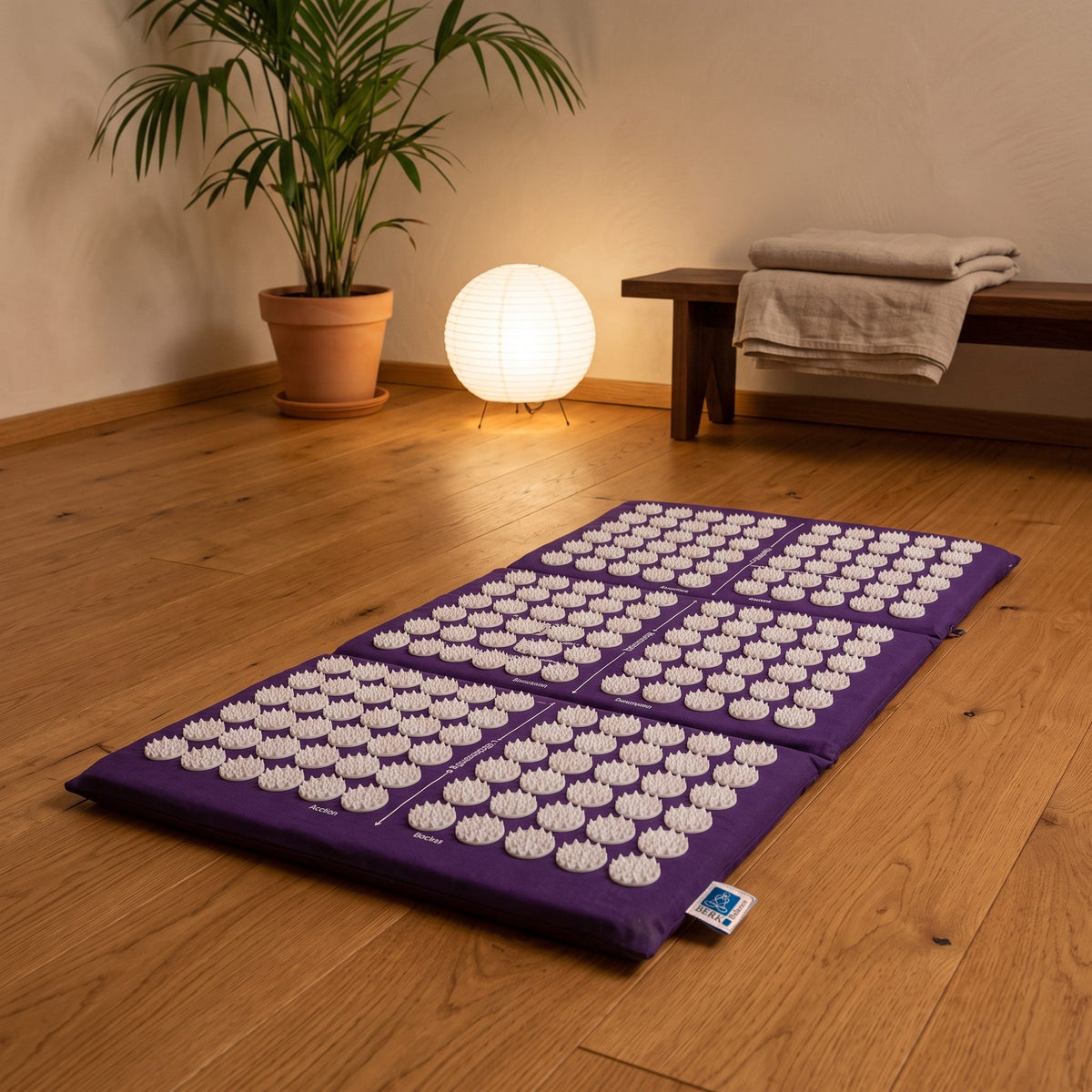 3-teilige Akupressurmatte für Reisen, 82 × 45 cm, Baumwollbezug lila, weiße Akupressurspitzen: ausgelegt auf dem Holzboden eines ruhigen Meditationsraums am Abend – Spirit of Gaia