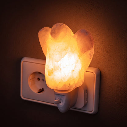 Salzkristall-Nachtlicht Engel in einer Steckdose leuchtet warm vor einer dunklen Putzwand