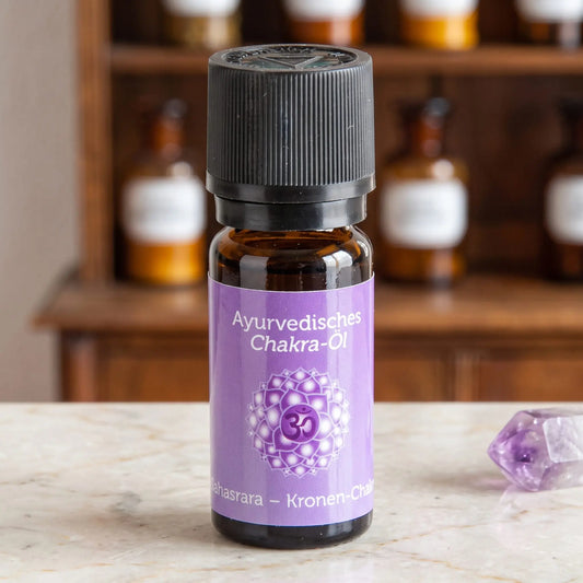 Ayurvedisches Chakra-Öl Sahasrara (Kronen-Chakra): 10-ml-Fläschchen aus Braunglas auf Marmortheke vor Apothekerschrank, daneben Amethyst – Spirit of Gaia