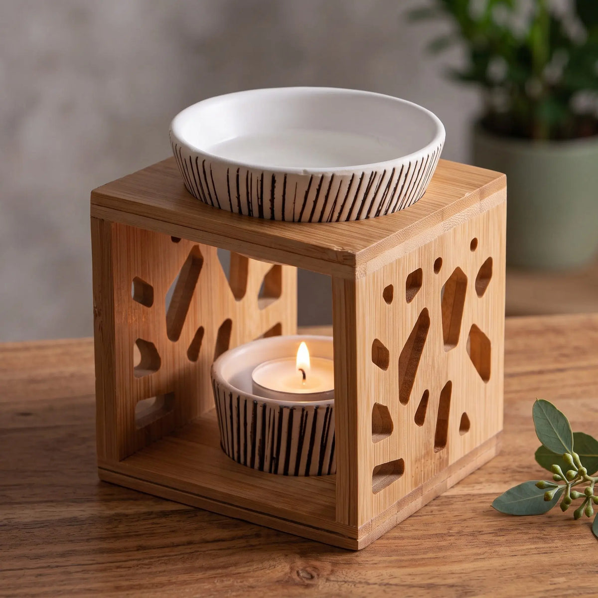Aromalampe Bambus & Keramik: mit brennendem Teelicht auf einem Holz-Sideboard im Wohnzimmer am Abend, daneben ein Eukalyptuszweig