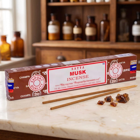 Satya Musk Räucherstäbchen: 15-g-Packung auf einer Marmortheke vor einem Apothekerschrank, daneben zwei lose Räucherstäbchen – Spirit of Gaia