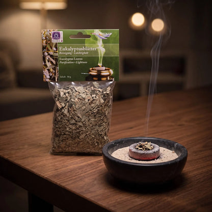 Eukalyptusblätter, sortenreines Räucherwerk von Berk, 50 g: eine Prise Eukalyptusblätter glimmt auf der Räucherkohle, dahinter die Tüte, feiner Rauch steigt auf einer dunklen Holzplatte am Abend auf – Spirit of Gaia