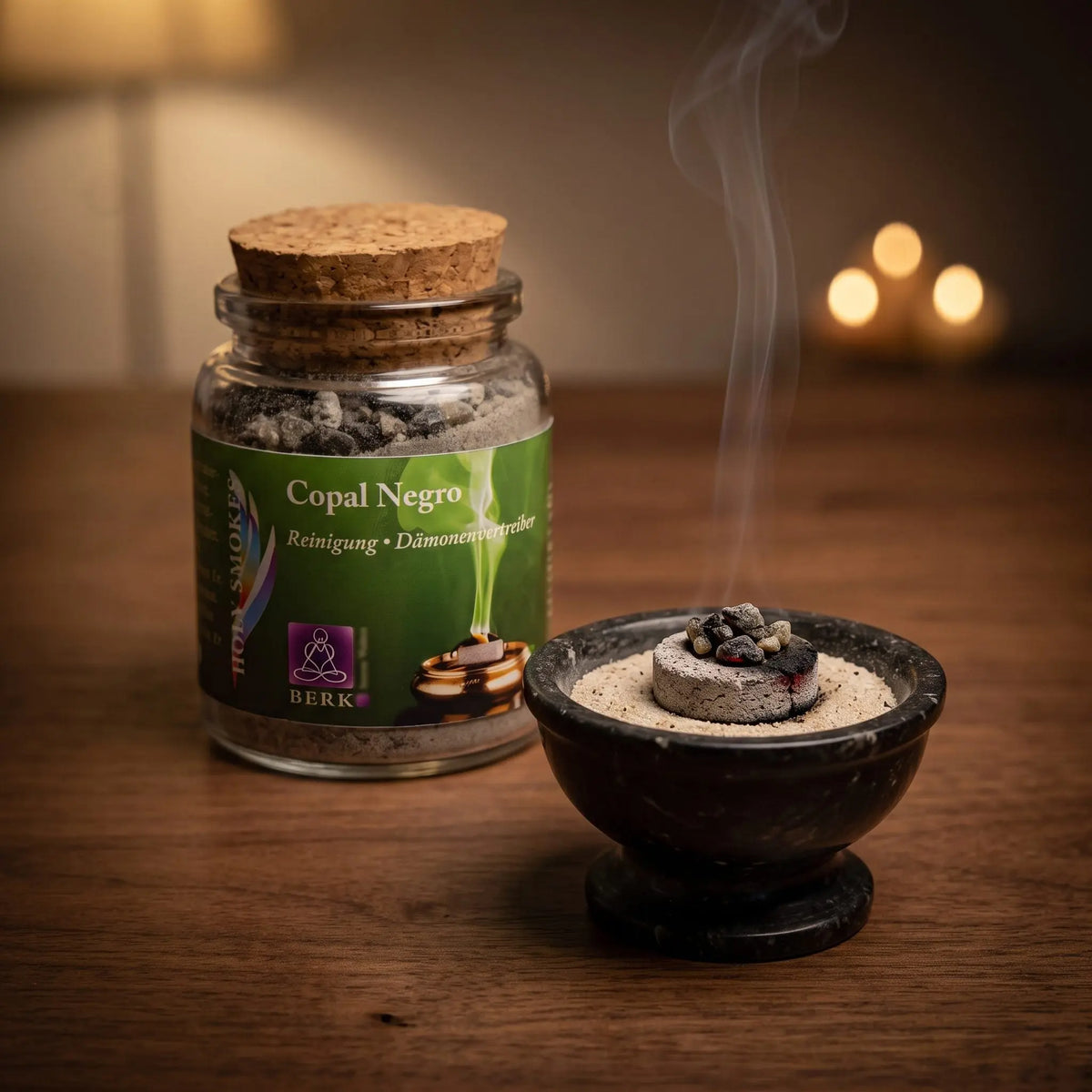 Copal Negro (Saumerio), reines Räucherharz von Berk, 60 ml im Korkglas: einige dunkle Copalstücke glimmen auf der Räucherkohle, dahinter das Korkglas, feiner Rauch steigt auf einer dunklen Holzplatte am Abend auf – Spirit of Gaia