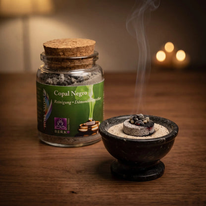 Copal Negro (Saumerio), reines Räucherharz von Berk, 60 ml im Korkglas: einige dunkle Copalstücke glimmen auf der Räucherkohle, dahinter das Korkglas, feiner Rauch steigt auf einer dunklen Holzplatte am Abend auf – Spirit of Gaia