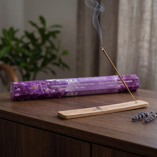 GR Royal Lavender Räucherstäbchen: glimmendes Räucherstäbchen mit feinem Rauch im Holzhalter, dahinter die Sechseck-Packung, auf einem Sideboard am Abend