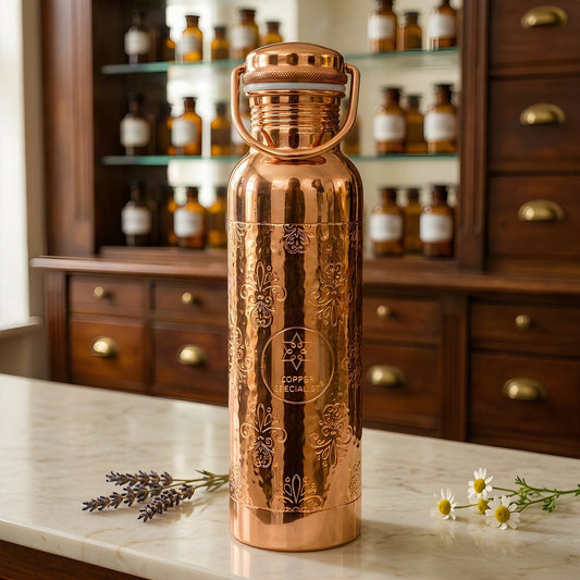 Polierte Kupfer-Trinkflasche mit graviertem Ziermuster und Bügelgriff auf Marmortheke vor Apothekerschrank – Spirit of Gaia