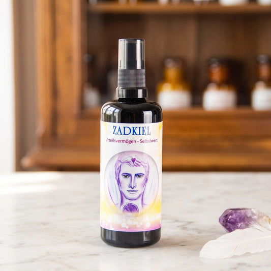 Seraphim Engel-Essenz Zadkiel: Aura-Spray in dunkler Violettglasflasche auf Marmortheke vor Apothekerschrank, daneben ein Amethyst und eine weiße Feder – Spirit of Gaia