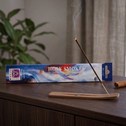 Zimt Räucherstäbchen Holy Smokes Blue Line: glimmendes Räucherstäbchen mit feinem Rauch im Holzhalter, dahinter die Packung, auf einem Sideboard am Abend