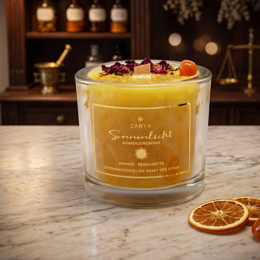 Zeremonie Kerze Sonnenlicht mit Karneol, Duft Orange und Bergamotte: Kerze im Glas auf der Marmortheke einer alten Apotheke am Abend, daneben zwei getrocknete Orangenscheiben und ein Karneol – Spirit of Gaia