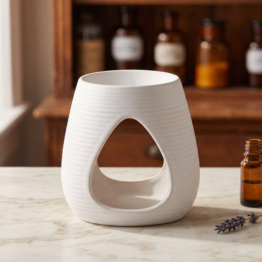 Aromalampe Pure White: weiße Keramik mit feinen Rillen auf Marmortheke vor Apothekerschrank, daneben ein Ölfläschchen und ein Lavendelzweig – Spirit of Gaia