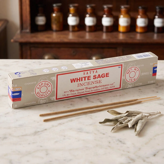 Satya White Sage Räucherstäbchen: 15-g-Packung auf einer Marmortheke vor einem Apothekerschrank, daneben zwei lose Räucherstäbchen – Spirit of Gaia