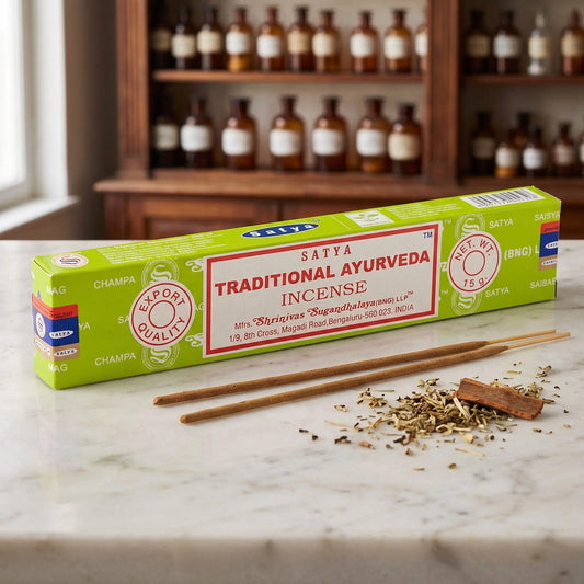 Satya Traditional Ayurveda Räucherstäbchen: 15-g-Packung auf einer Marmortheke vor einem Apothekerschrank, daneben zwei lose Räucherstäbchen – Spirit of Gaia