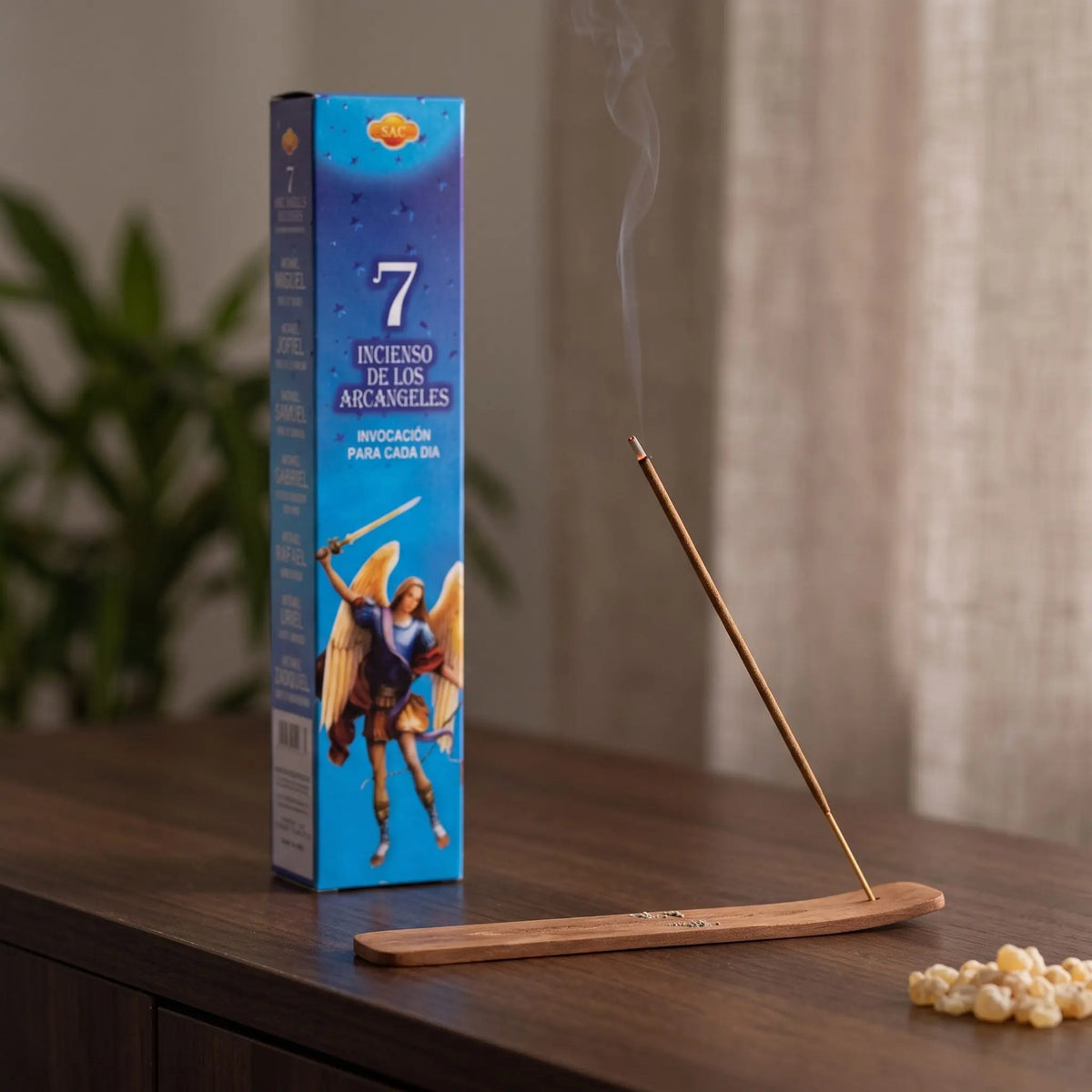 Räucherstäbchen 7 Erzengel: glimmendes Räucherstäbchen mit feinem Rauch im Holzhalter, dahinter die Packung, auf einem Sideboard am Abend