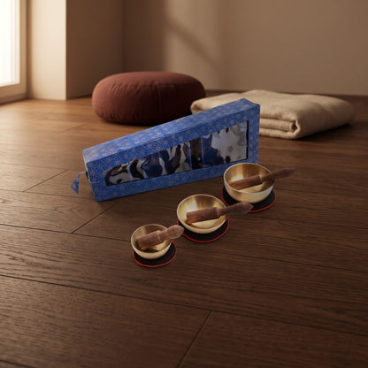 Klangschalen-3er-Set mit blauer Box und drei Schalen auf Unterlagen auf dem Holzboden eines Meditationsraums