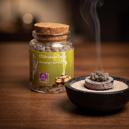 Olibanum India, reiner Weihrauch von Berk, 60 ml im Korkglas: glimmende Räucherkohle mit zwei Weihrauchtränen in einer Specksteinschale, dahinter das Korkglas, feiner Rauch steigt auf einer dunklen Holzplatte am Abend auf – Spirit of Gaia