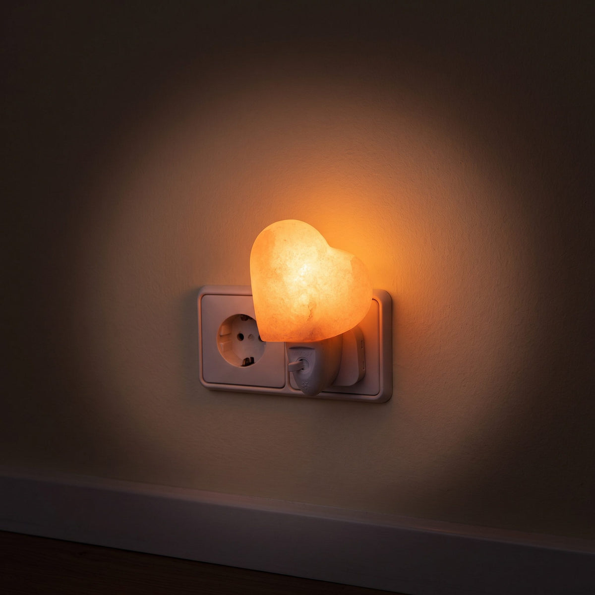 Das Salzkristall-Nachtlicht Herz in der Steckdose eines dunklen Flurs, das Licht bildet einen weichen Kreis auf der Wand