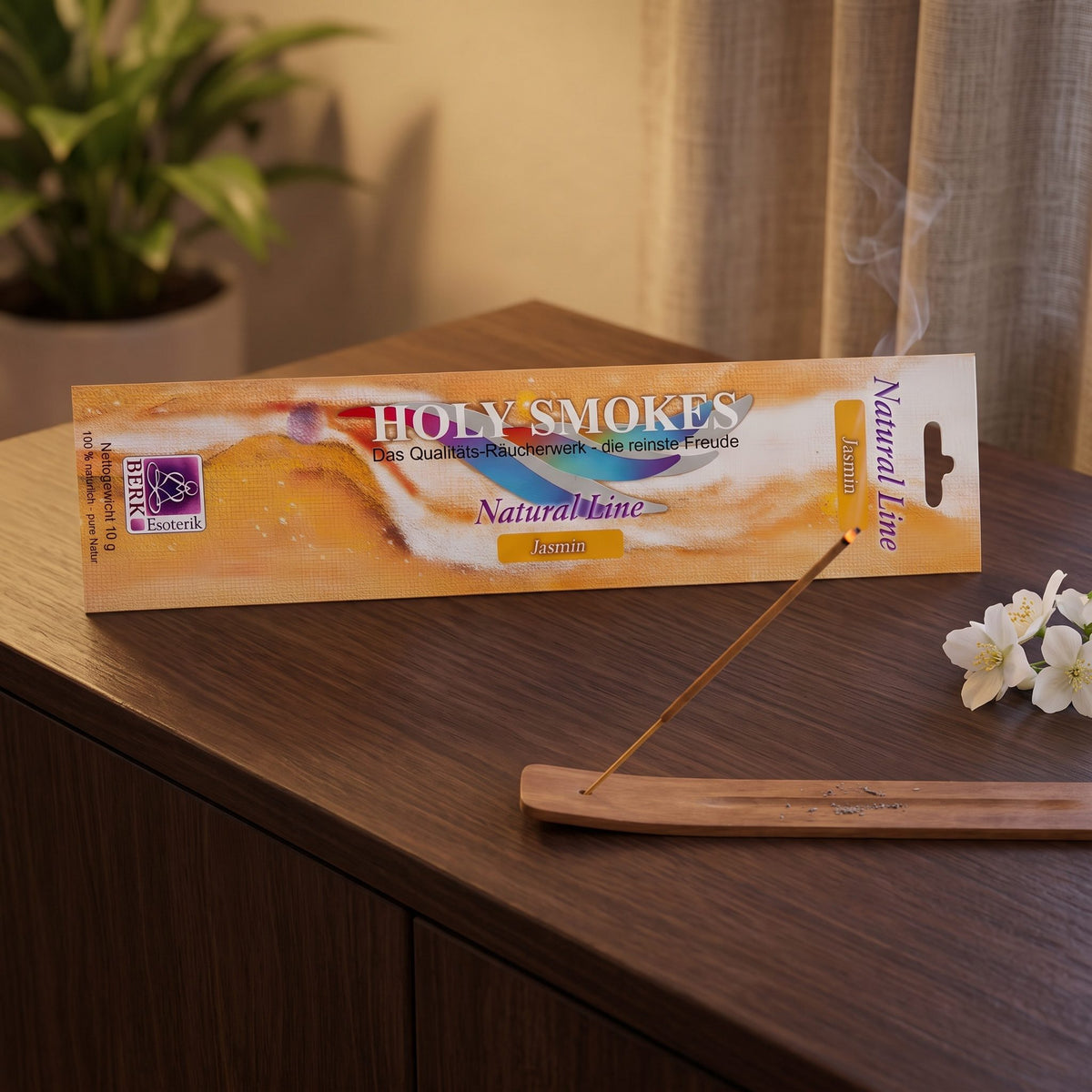 Jasmin Räucherstäbchen Natural Line: glimmendes Stäbchen im Holzhalter auf einem dunklen Sideboard, dahinter die Packung, am Abend