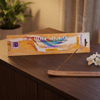 Jasmin Räucherstäbchen Natural Line: glimmendes Stäbchen im Holzhalter auf einem dunklen Sideboard, dahinter die Packung, am Abend