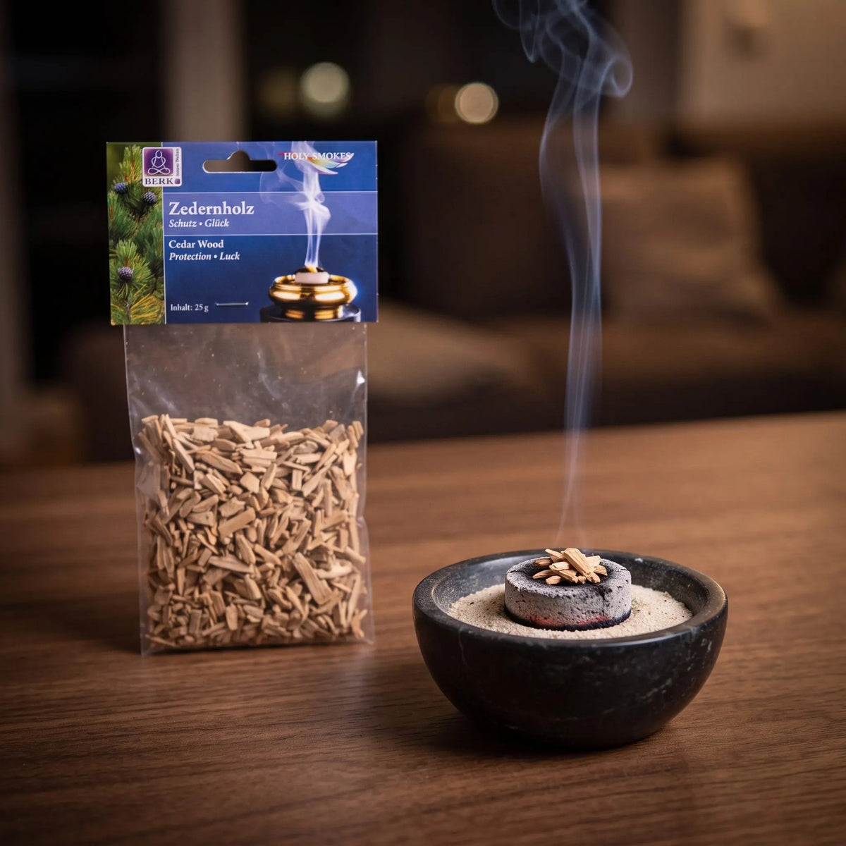 Zedernholz, sortenreines Räucherwerk von Berk, 25 g: einige Zedernholzspäne glimmen auf der Räucherkohle, dahinter die Tüte, feiner Rauch steigt auf einer dunklen Holzplatte am Abend auf – Spirit of Gaia
