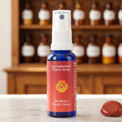 Ayurvedisches Chakra-Spray Muladhara (Wurzel-Chakra): 30-ml-Sprühflasche aus blauem Glas auf Marmortheke vor Apothekerschrank, daneben roter Jaspis – Spirit of Gaia
