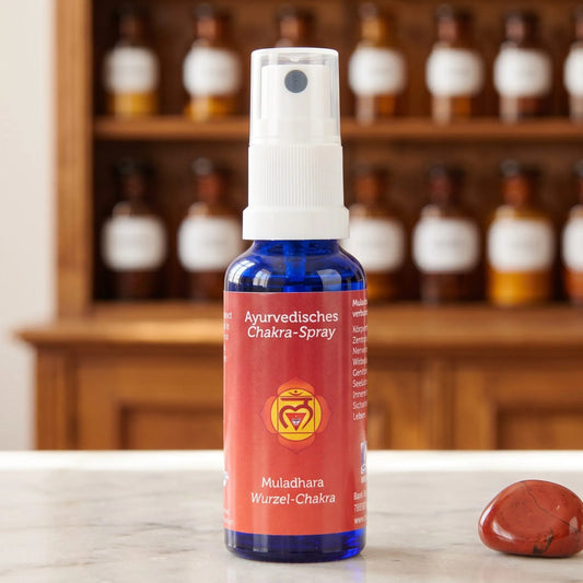Ayurvedisches Chakra-Spray Muladhara (Wurzel-Chakra): 30-ml-Sprühflasche aus blauem Glas auf Marmortheke vor Apothekerschrank, daneben roter Jaspis – Spirit of Gaia
