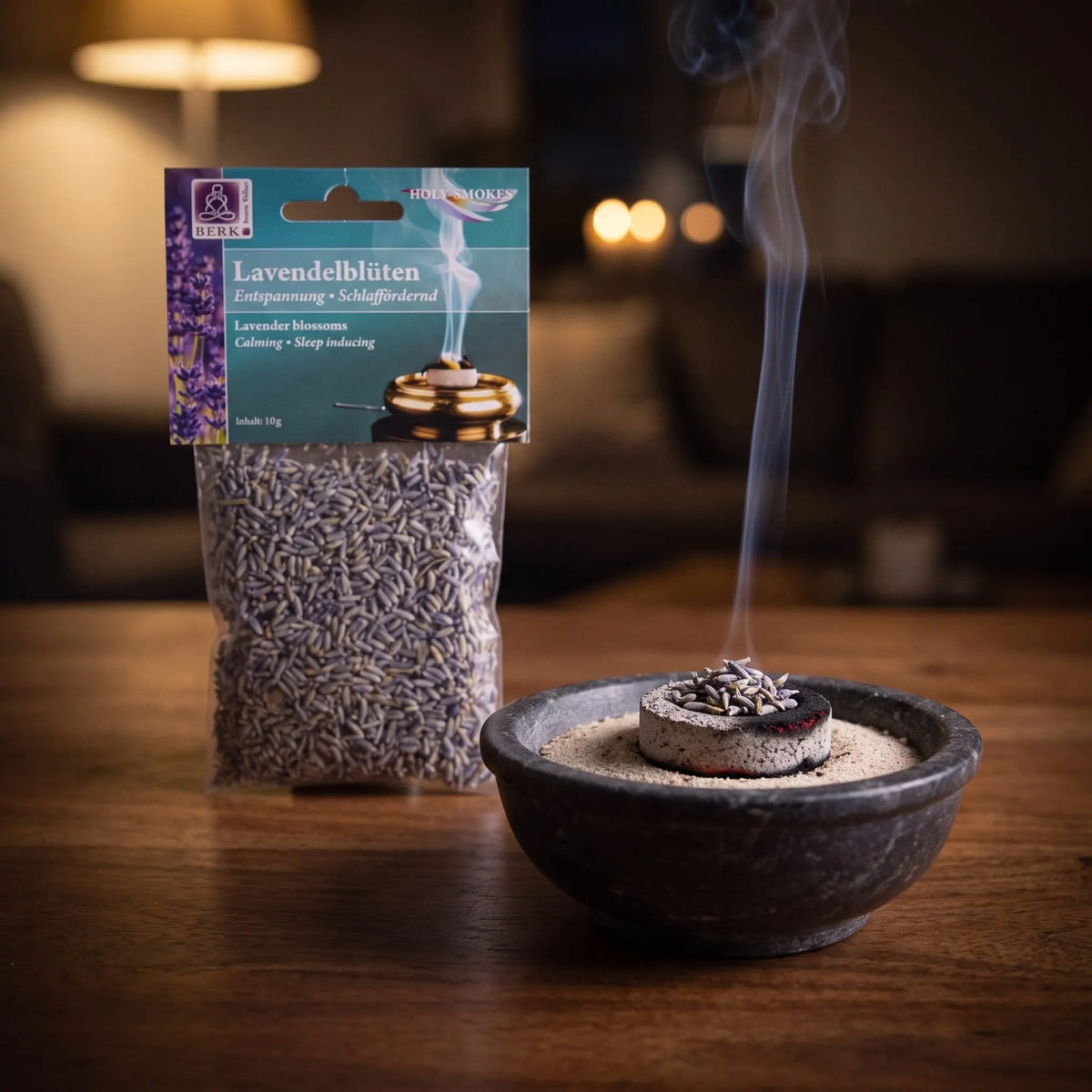 Lavendelblüten, sortenreines Räucherwerk von Berk, 10 g: eine Prise Lavendelblüten glimmt auf der Räucherkohle, dahinter die Tüte, feiner Rauch steigt auf einer dunklen Holzplatte am Abend auf – Spirit of Gaia